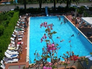 Une piscine rectangulaire où des personnes nagent et se détendent au bord de l’eau.