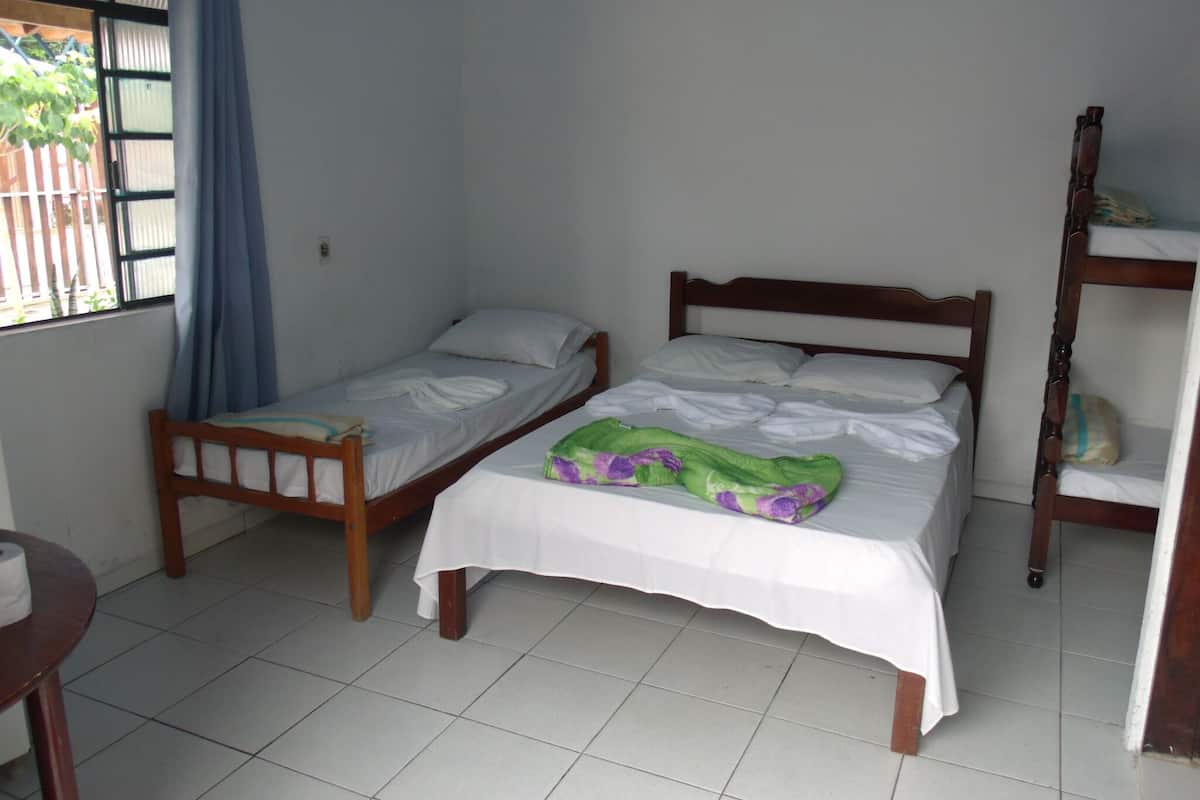 A small, clean room with two wooden beds, a tiled floor, and a window with curtains.