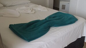 Un llit amb llençols blancs i una manta color esmeralda, una almoinada blanca i una tovallola blanca sobre el llit.
