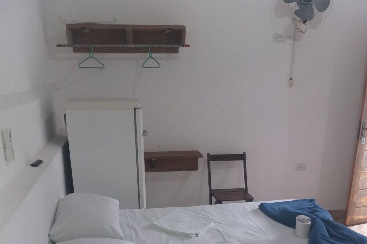 A bedroom with a bed, a small table, a chair, a fan, and a shelf.