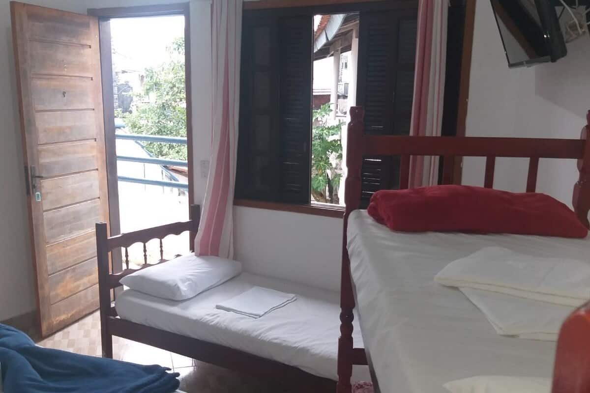 A room with two beds, a television mounted on the wall, and an air conditioning unit above the window.