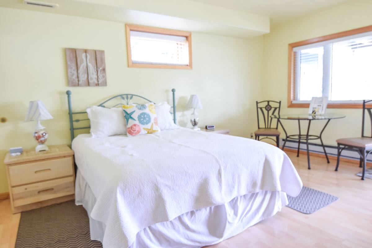 A bedroom with a bed, bedside tables, a chair, a desk, and a window.