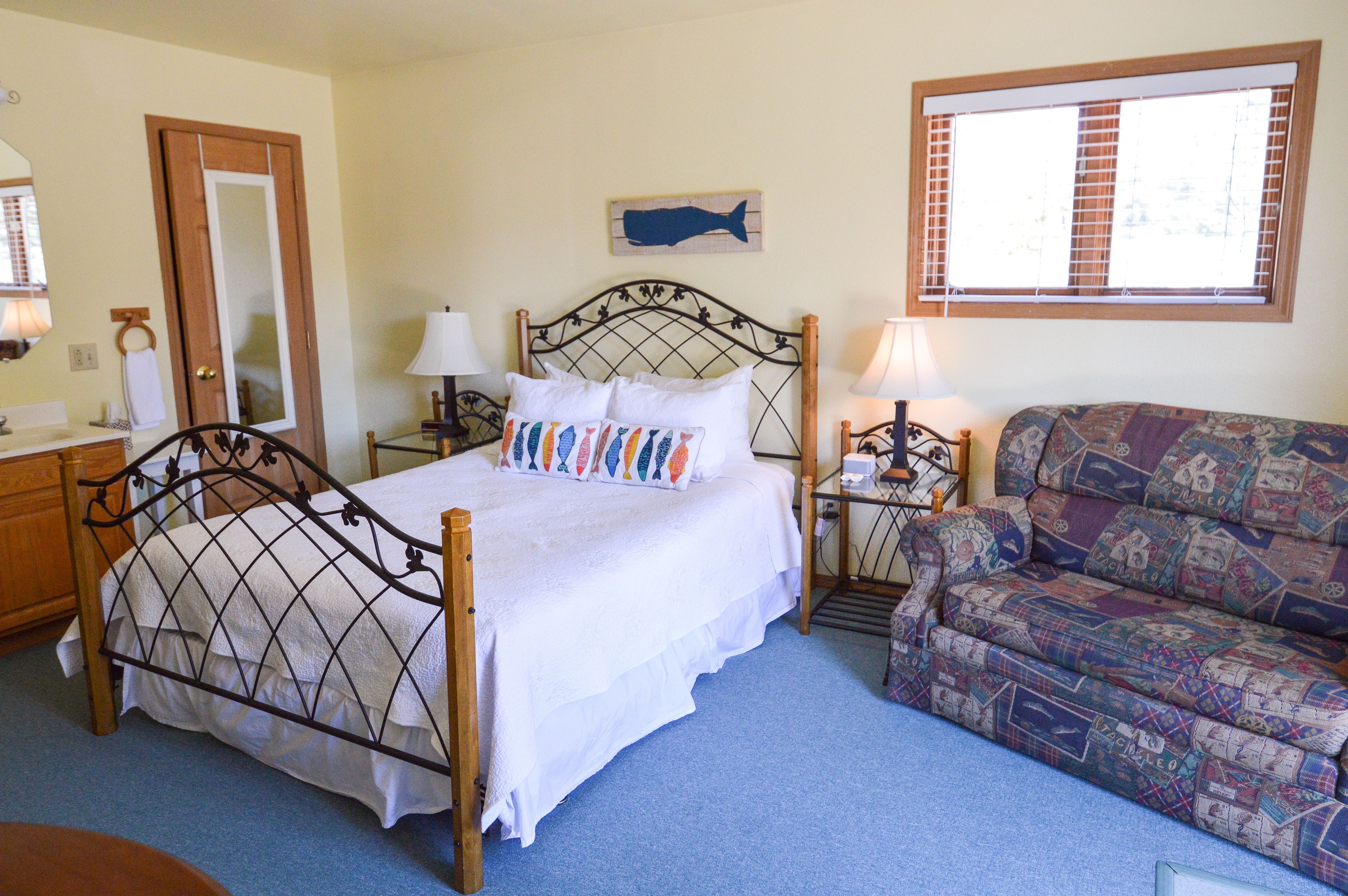 A bedroom with a bed, bedside tables, a chair, a window, and a fish artwork on the wall.