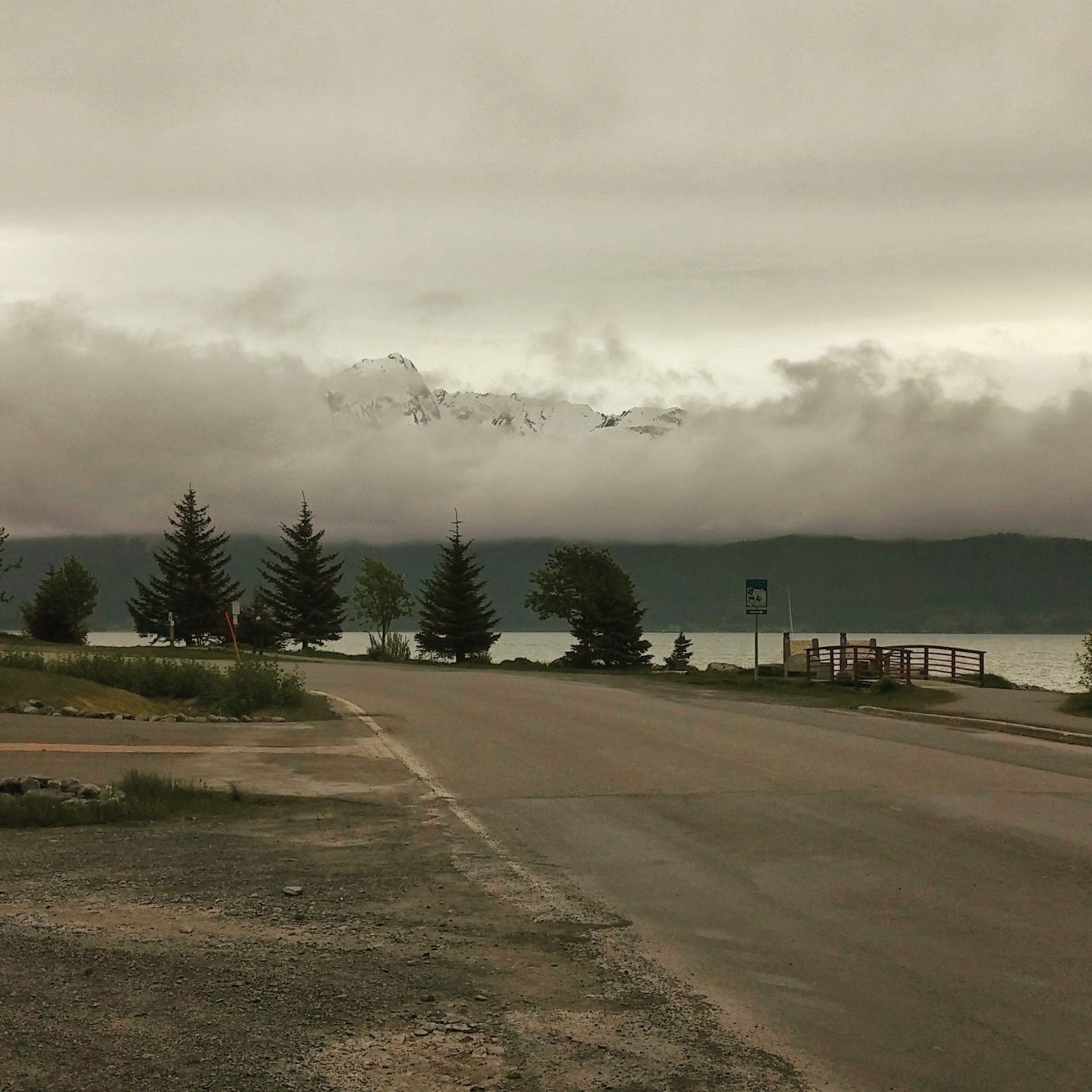 A road leading to a body of water with a mountain in the background and a signpost on the right.