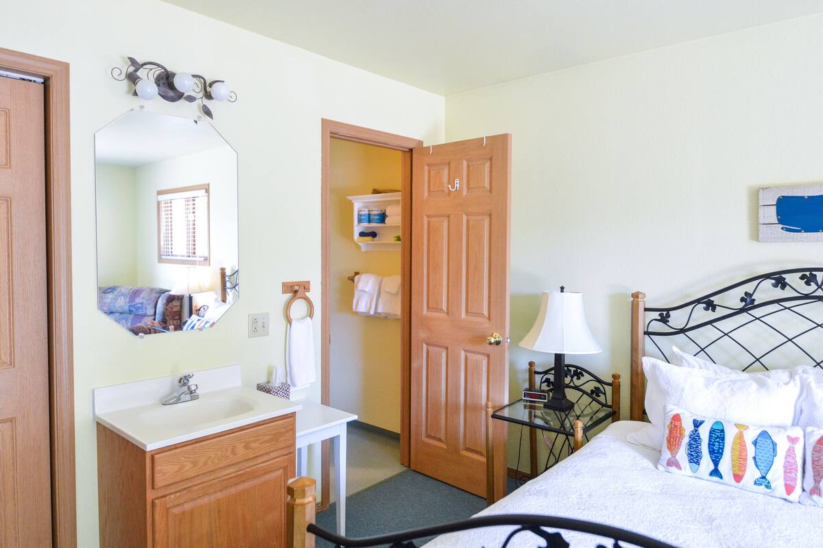A bedroom with a bed, bedside table, lamp, and a mirror.