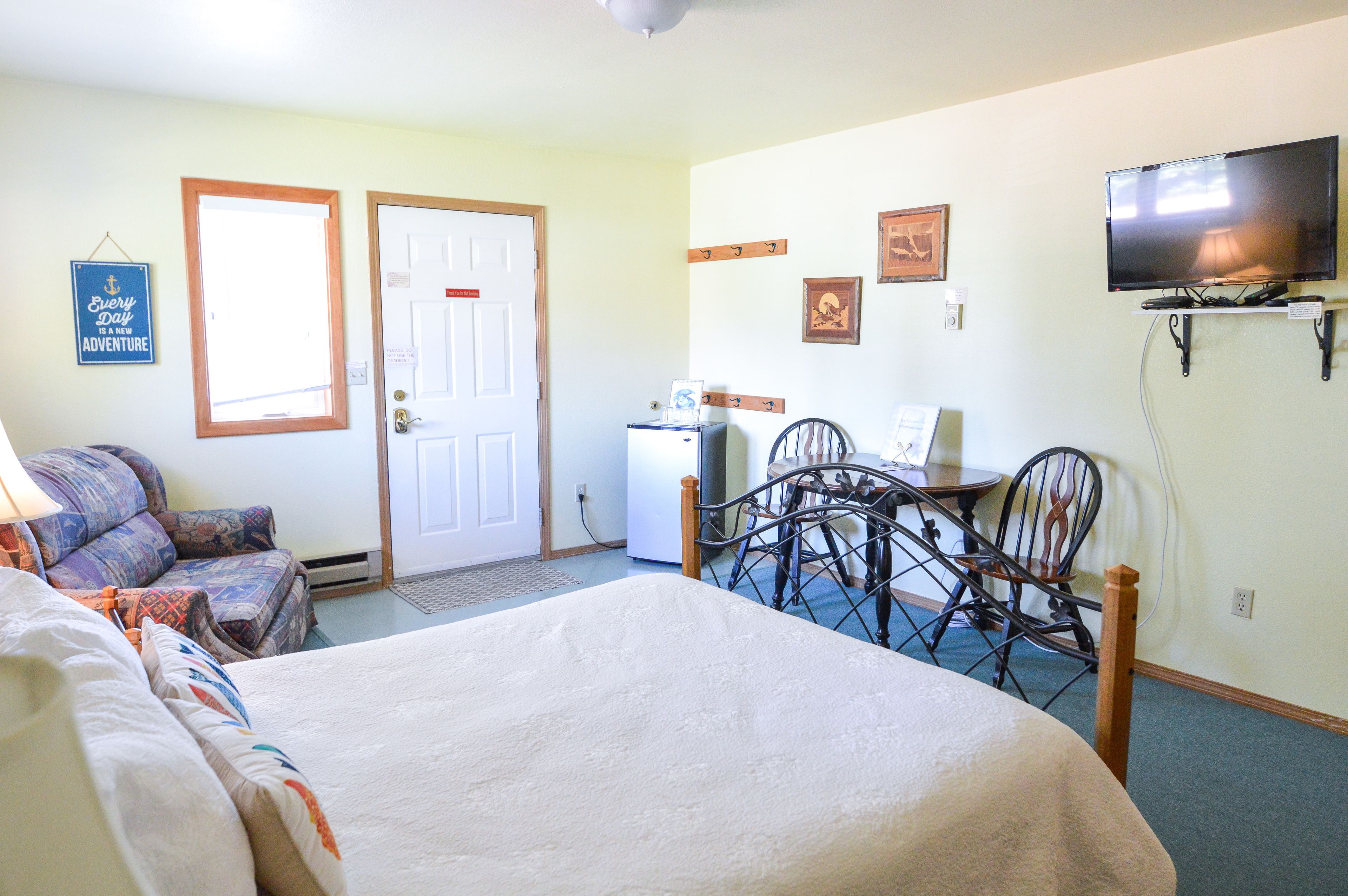 A hotel room with a bed, a desk with a chair, a television, and a refrigerator.