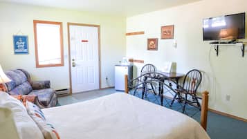 A hotel room with a bed, a desk with a chair, a television, and a refrigerator.
