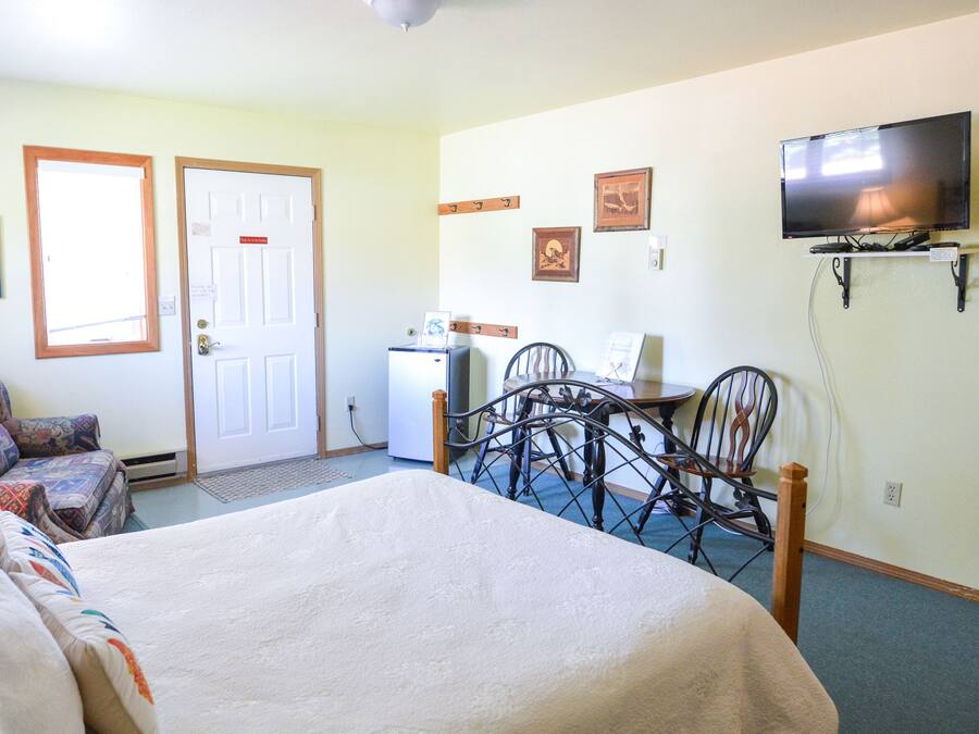 A hotel room with a bed, a desk with a chair, a television, and a refrigerator.
