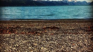 Una playa de guijarros con un lago y montañas al fondo.