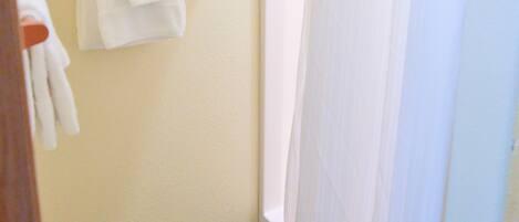 A bathroom with a towel rack holding two white towels, a shower curtain, and a window.