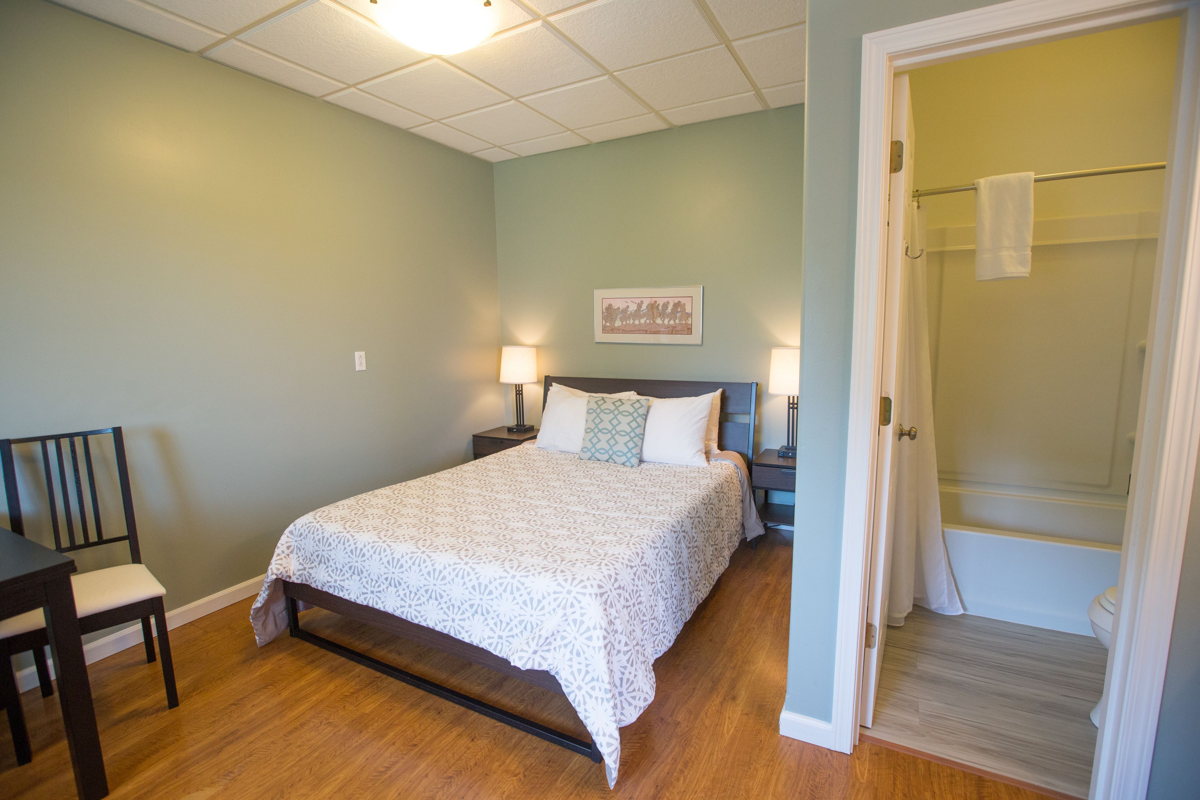 A bedroom with a bed, bedside tables, a chair, and a bathroom with a shower curtain.