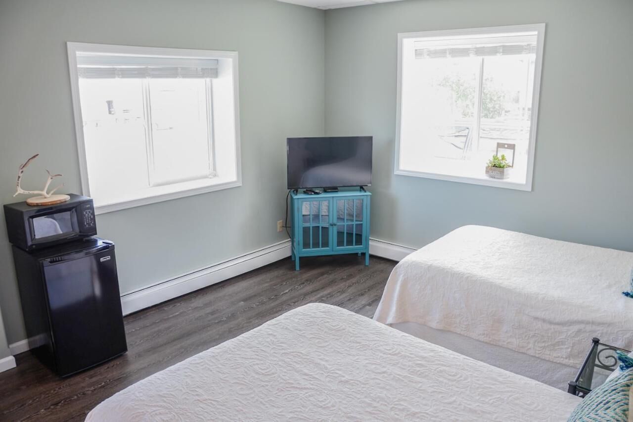 A room with two beds, a TV on a stand, a small fridge, and a window with a view.
