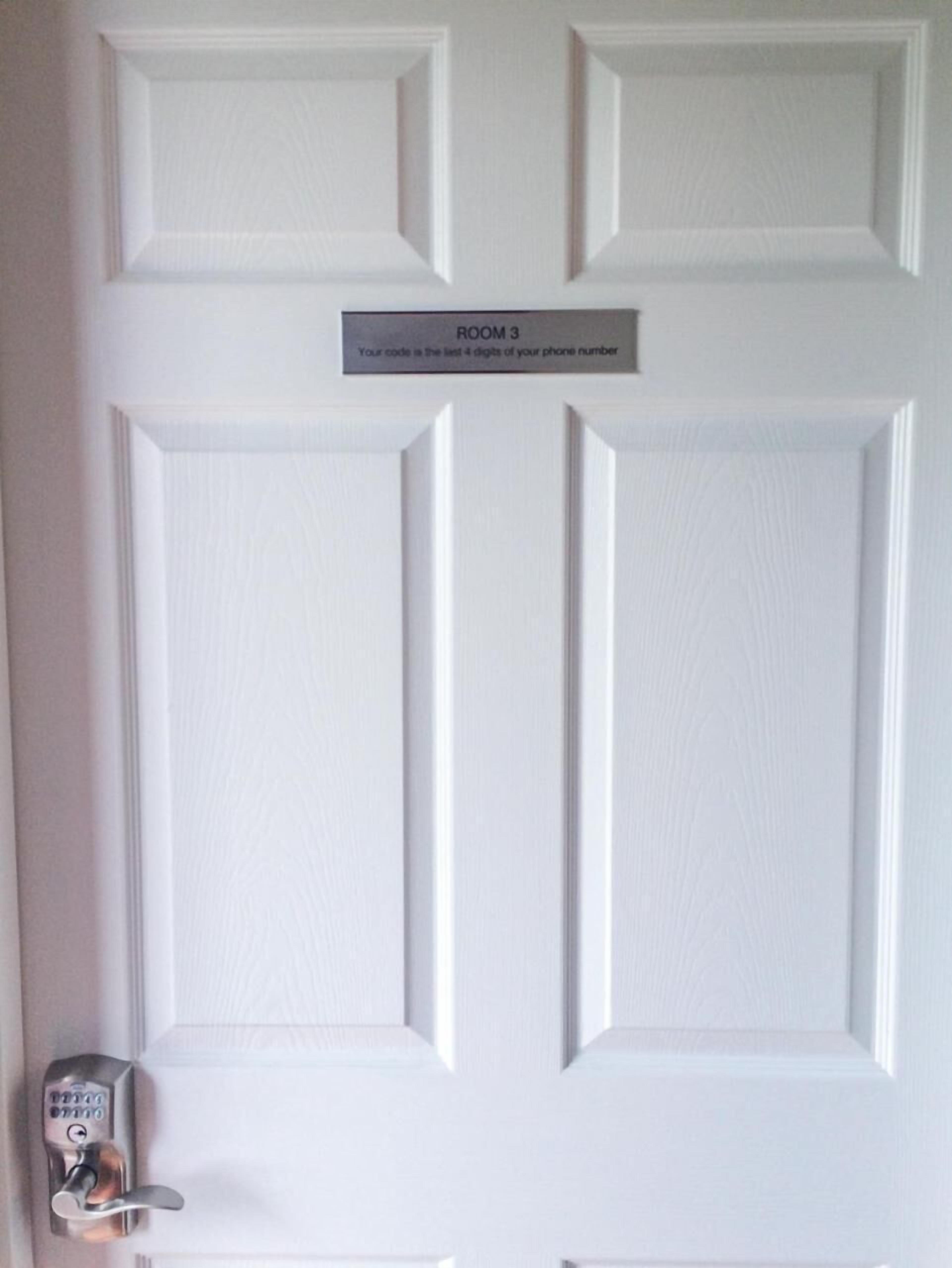 A white door with a keypad lock and a sign above it that reads "ROOM 3 Your code is the last 4 digits of your phone number."