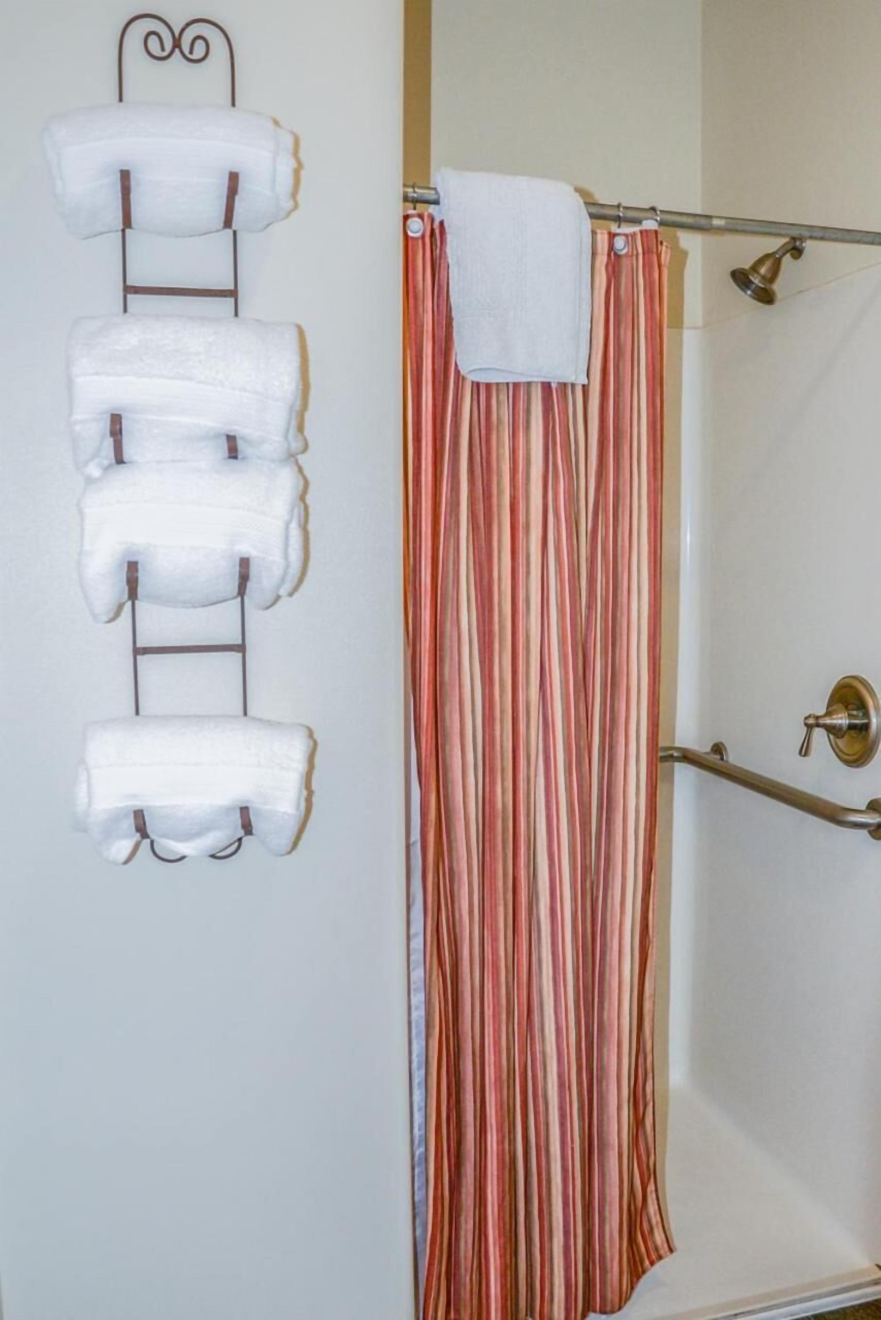 Een badkamer met een handdoekrek met vier witte handdoeken, een gestreepte douchegordijn en een douchedeur.