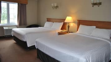 A hotel room with two beds, a desk with a lamp, and a window with curtains.