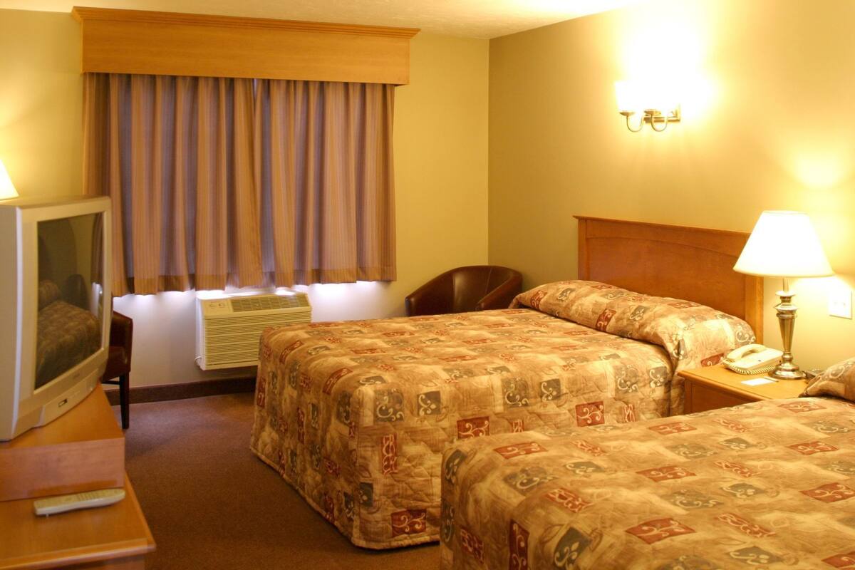 Habitación de hotel con dos camas, televisor, escritorio con lámpara, una silla y ventana con cortinas.