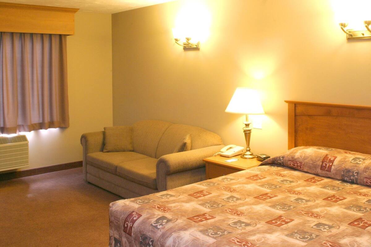 Una habitación de hotel con una cama, una silla, una mesita de noche con lámpara y un teléfono.