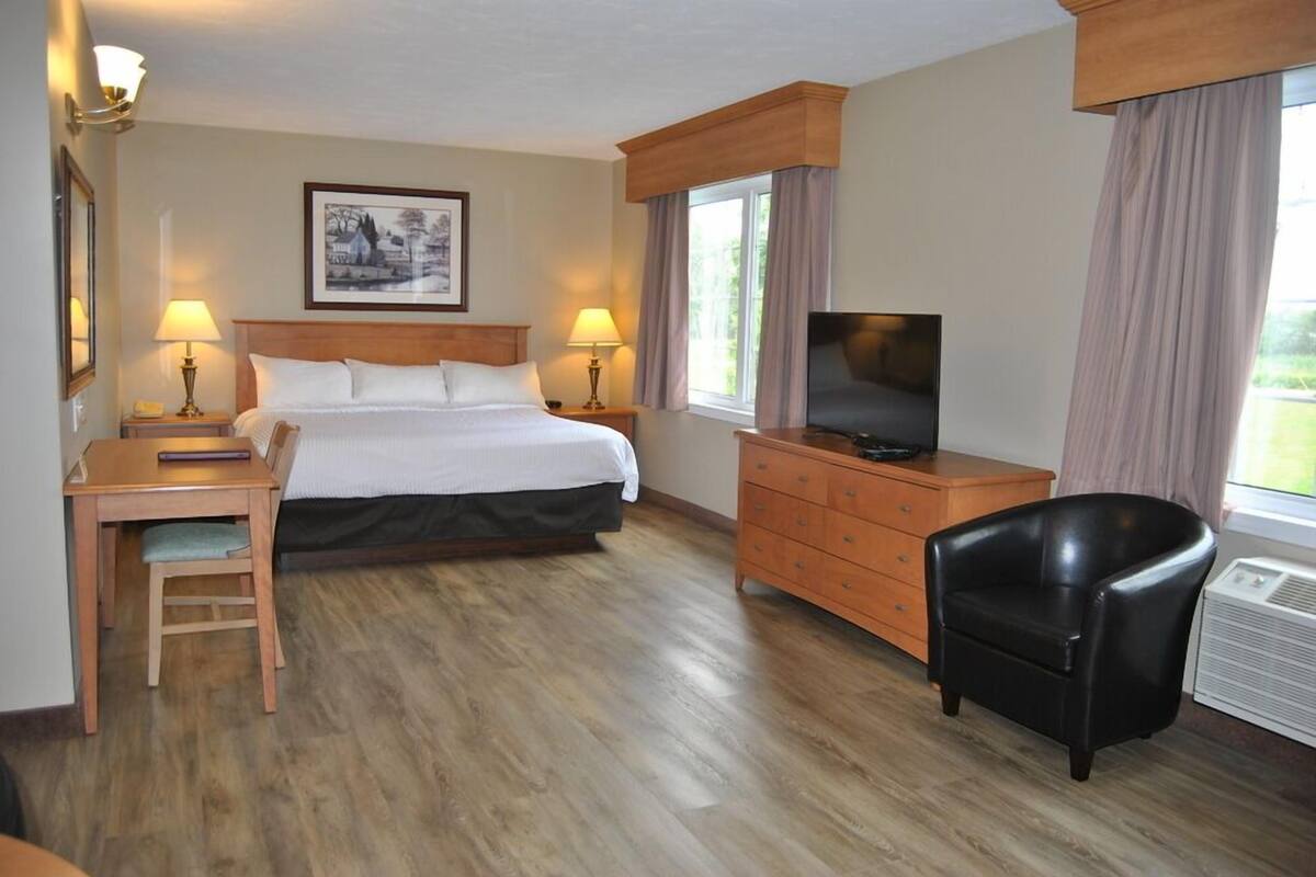 Habitación de hotel con cama, escritorio, silla, cómoda, televisor y ventana con cortinas.