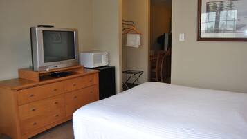 Een hotelkamer met een bed, een houten dressoir met televisie en magnetron, een stoel en een inlijsting foto aan de muur.