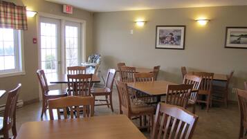 A dining area with wooden tables and chairs, a high chair, and exit signs.