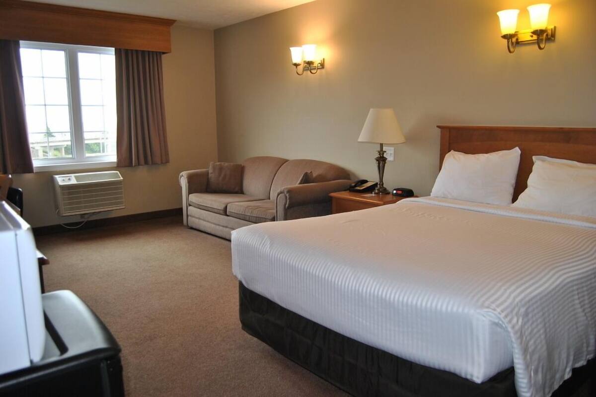 Habitación de hotel con una cama grande, un sofá, un escritorio con lámpara y una ventana con cortinas.