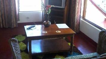 Una sala de estar con una mesa de centro de madera, un televisor sobre un mueble de madera y una ventana con cortinas.