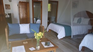 A room with a sofa, two single beds, a wooden coffee table with a vase of flowers, and a patterned rug. - LTU Garden (Negril)