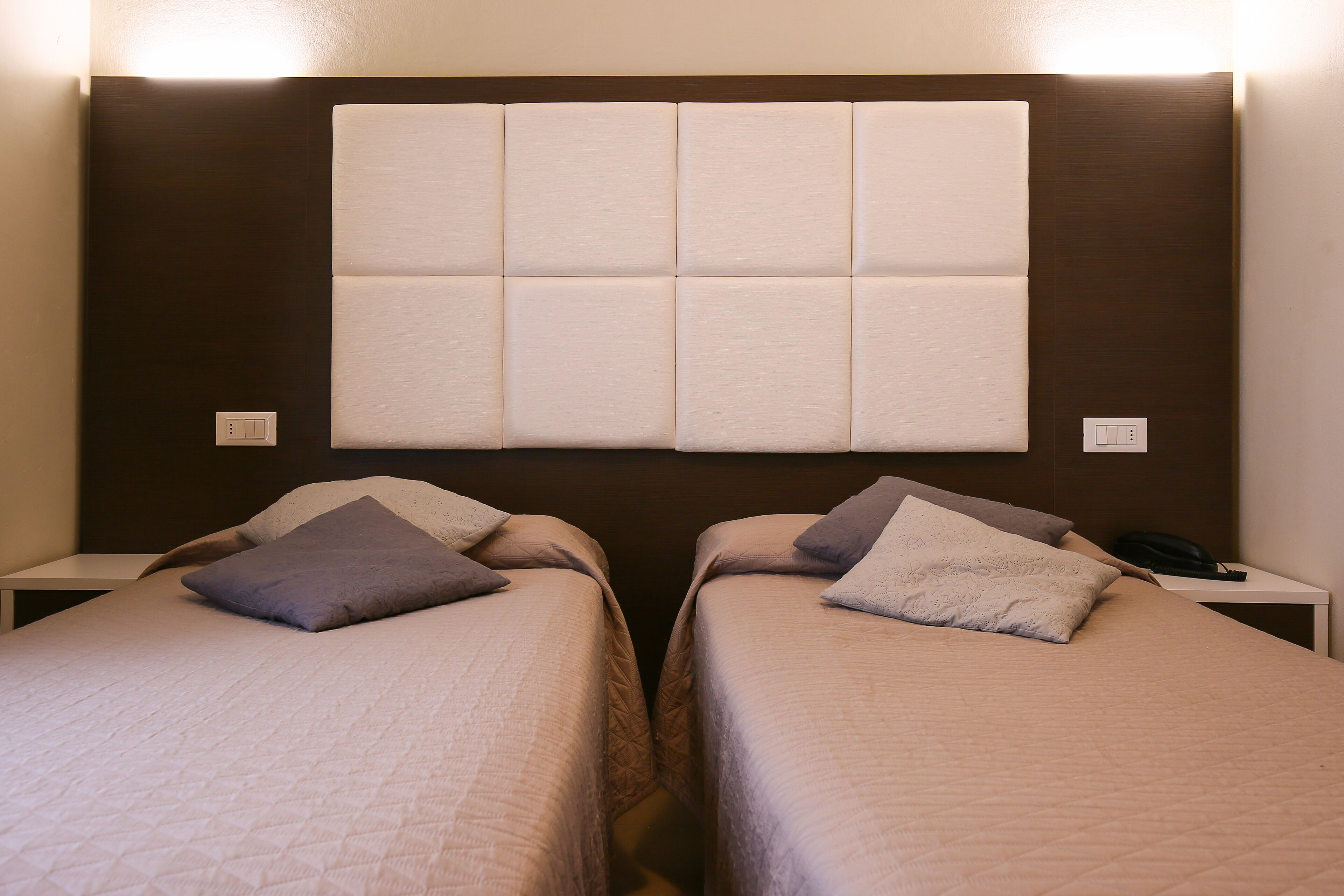A hotel room with two single beds, each with a pillow and a bedside table.