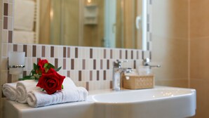 Une salle de bain avec un lavabo blanc, un miroir et un porte-serviettes sur lequel sont pliées des serviettes, ainsi qu’une rose rouge.