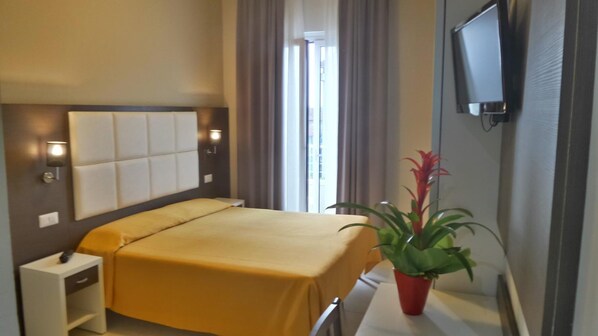 Habitación de hotel con cama, mesita de noche, televisión y una planta en maceta.
