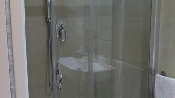 Eine Duschkabine mit Glaswänden, einer Handbrause und einem am Wand montierten Wasserhahn.