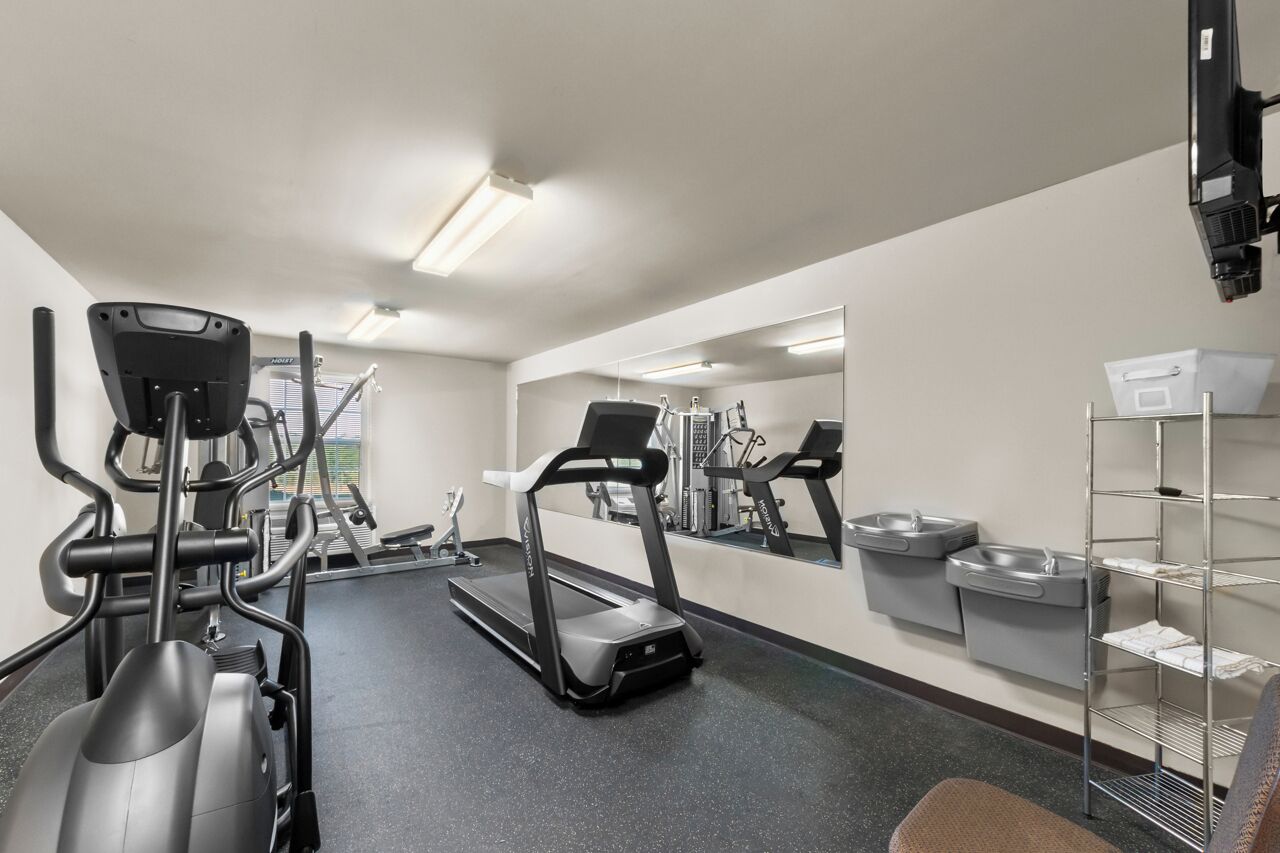 Un gimnasio con cintas de correr, elípticas y un espejo grande.