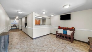 A spacious hallway with a kitchen area, a bench with pillows, and a mounted TV. - Risewell Kitchen Suites Pleasanton (Pleasanton)