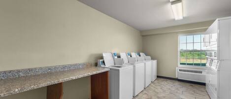 A laundry room with a granite countertop, multiple washing machines, and a large window providing a view of the outdoors.