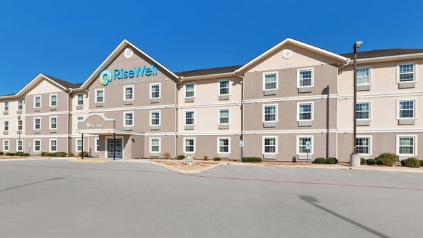 A multi-story hotel with a 'Welcome' sign at the entrance, featuring a modern design with beige and white color scheme. - Risewell Kitchen Suites Pleasanton (Pleasanton)
