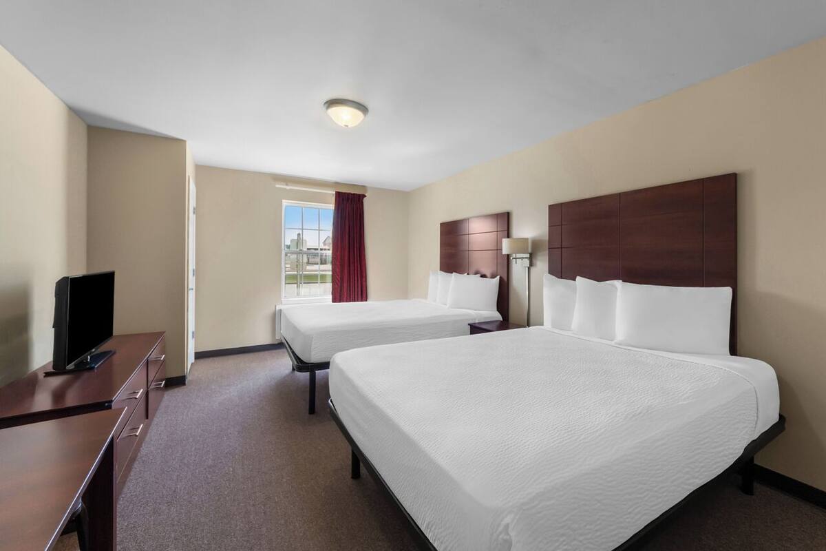 Une chambre d’hôtel avec deux lits, un bureau, une télévision et une fenêtre donnant sur un beau paysage.
