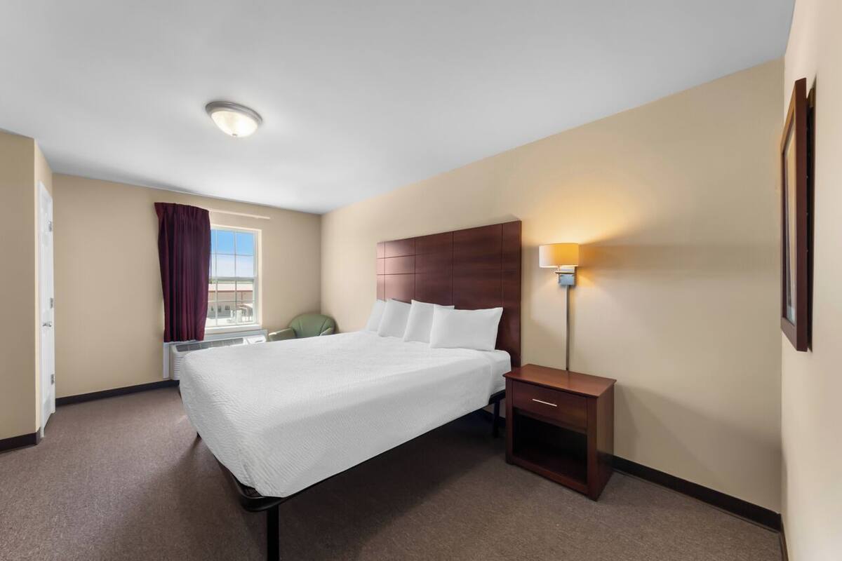Une chambre d’hôtel avec un grand lit, une table de chevet, une lampe, une fenêtre avec des rideaux et une porte.