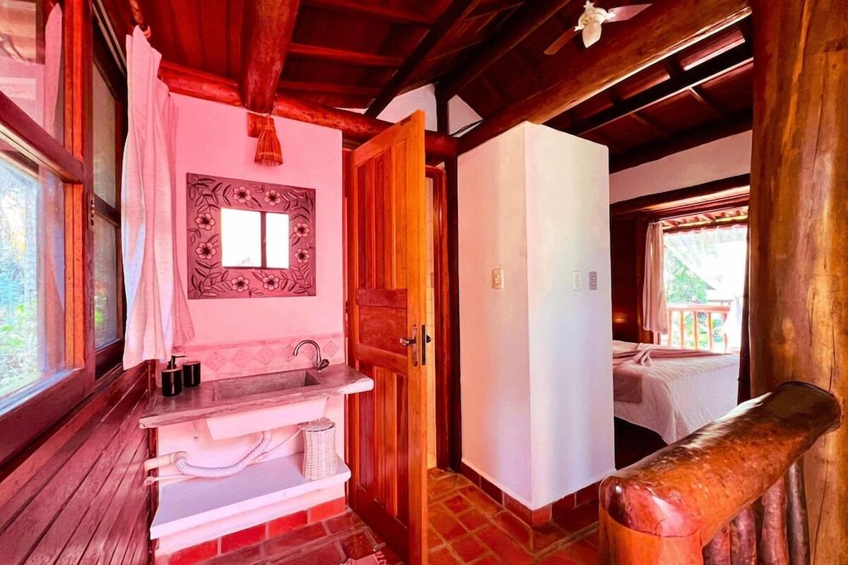 A wooden interior with a bathroom, a bed, and a view of the outdoors.