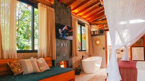 Une chambre moderne avec un grand lit, un coin salon, une baignoire et un téléviseur fixé au mur.