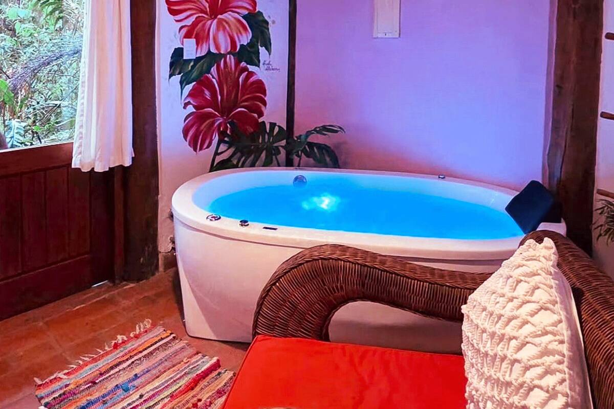 A room with a hot tub, wicker furniture, a colorful rug, and a painting of flowers.