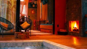 Une pièce dotée d’un jacuzzi, d’un plancher en bois, d’une cheminée et de deux fauteuils noirs avec des coussins.