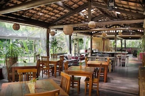 An indoor dining area with wooden tables and chairs, a bar area, and large windows allowing natural light. - Smart Hotel Reserva Camburi (São Sebastião)