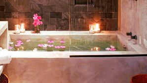 Une salle de bain avec un mur en pierre, une baignoire décorée de fleurs roses et des bougies.