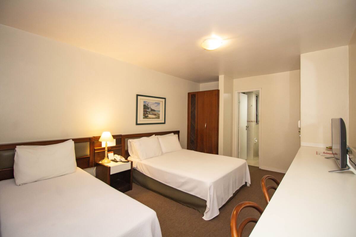 Une chambre d’hôtel avec deux lits, un bureau, une chaise, une télévision et un tableau encadré au mur.
