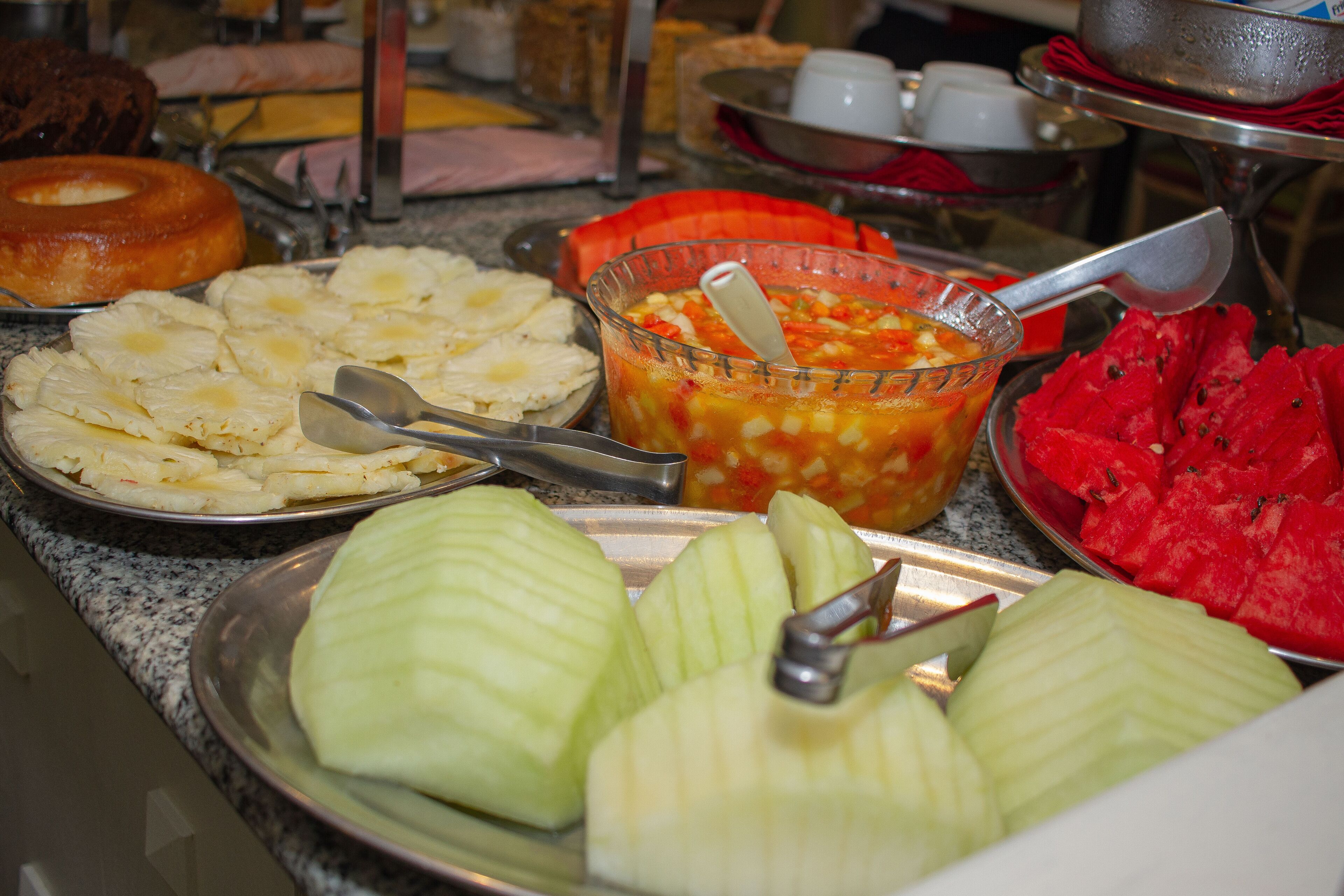 Buffet variado con opciones de comida, incluyendo piña, sandía y una ensalada de frutas.