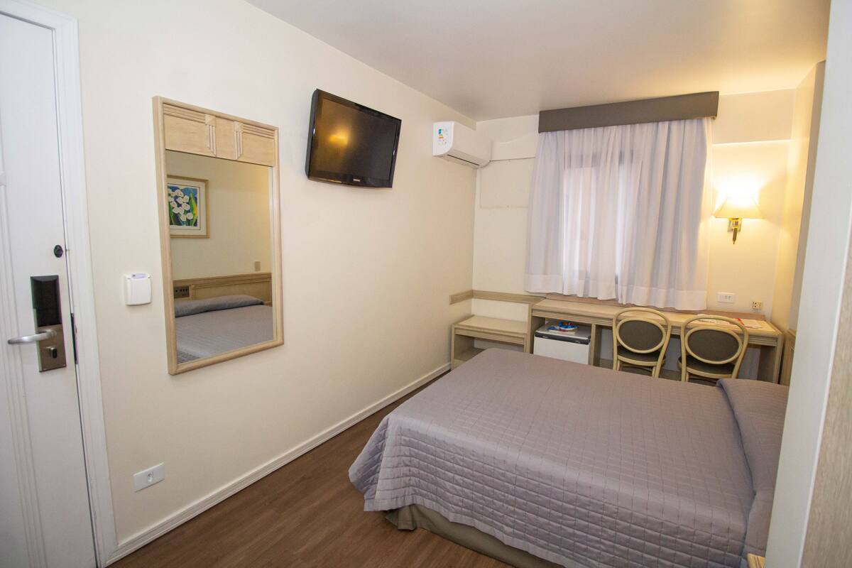 Une chambre d’hôtel comprenant un lit, un bureau, deux chaises, une télévision et un miroir.