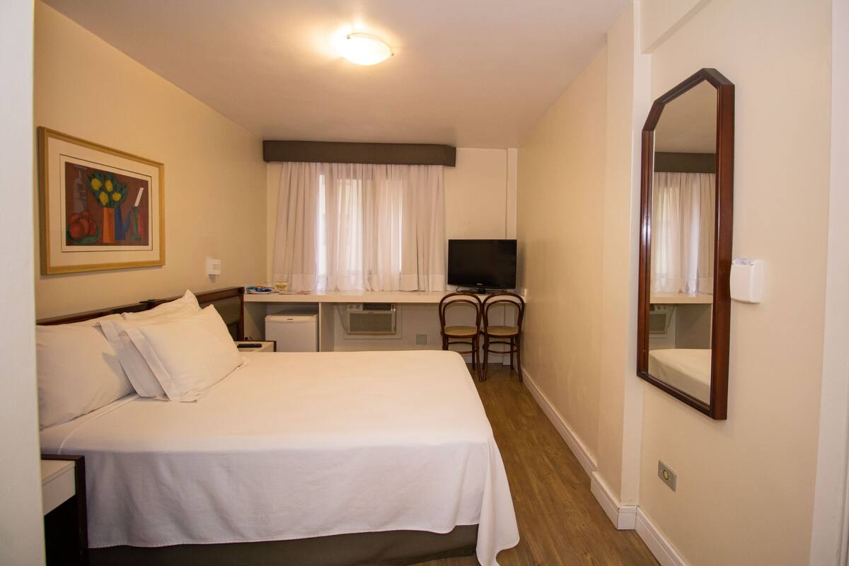 Une chambre d’hôtel comprenant un lit, un bureau avec une chaise, une télévision et un grand miroir.
