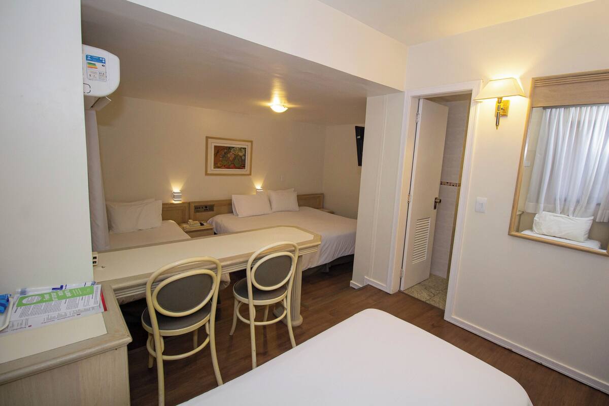 Une chambre d’hôtel avec un lit, deux chaises, un bureau, un miroir et un tableau au mur.