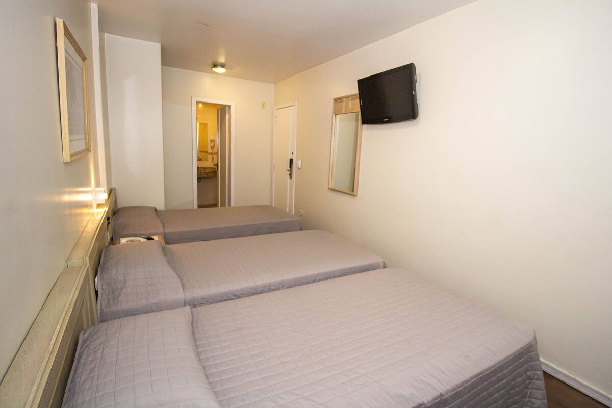 Une chambre d’hôtel avec trois lits, un téléviseur fixé au mur et une porte donnant sur une salle de bain.