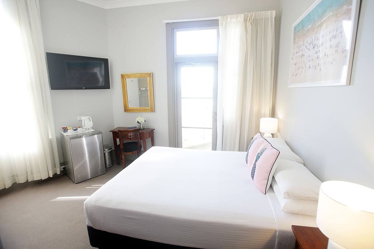 A hotel room with a bed, a desk, a chair, a TV, a window, and a door.